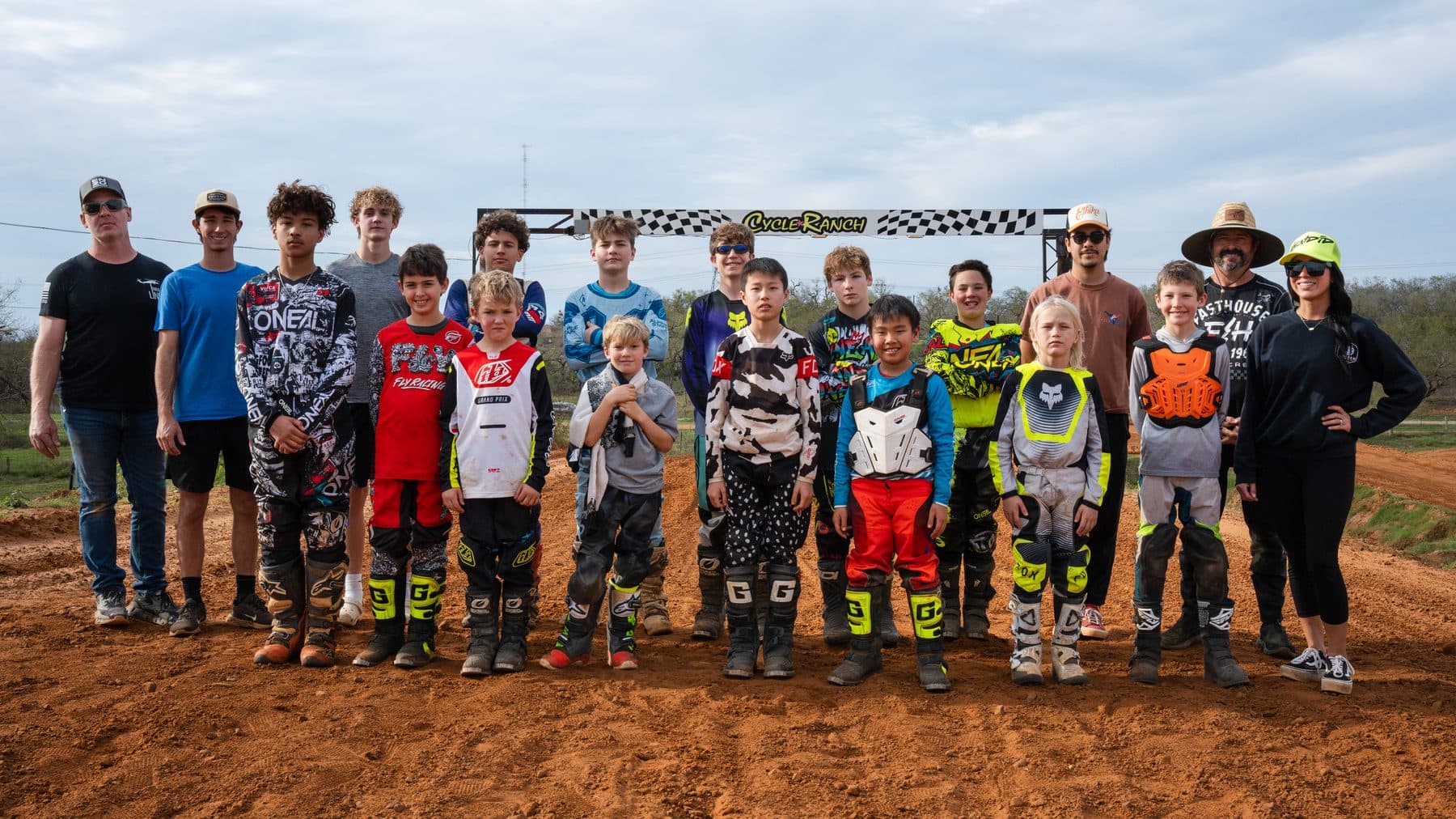 A large group of riders of all ages posing together under the Cycle Ranch banner on the track