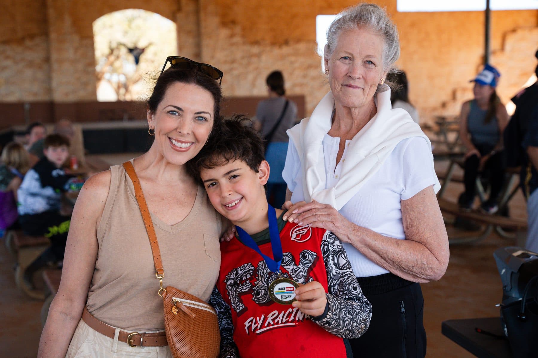 A mother, son and grandmother smiling together as the boy shows off his race medal in the Cycle Ranch pavilion