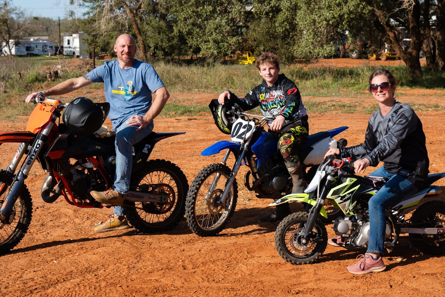 A dad, son and mom sitting on their dirt bikes together on a sunny ride day at Cycle Ranch
