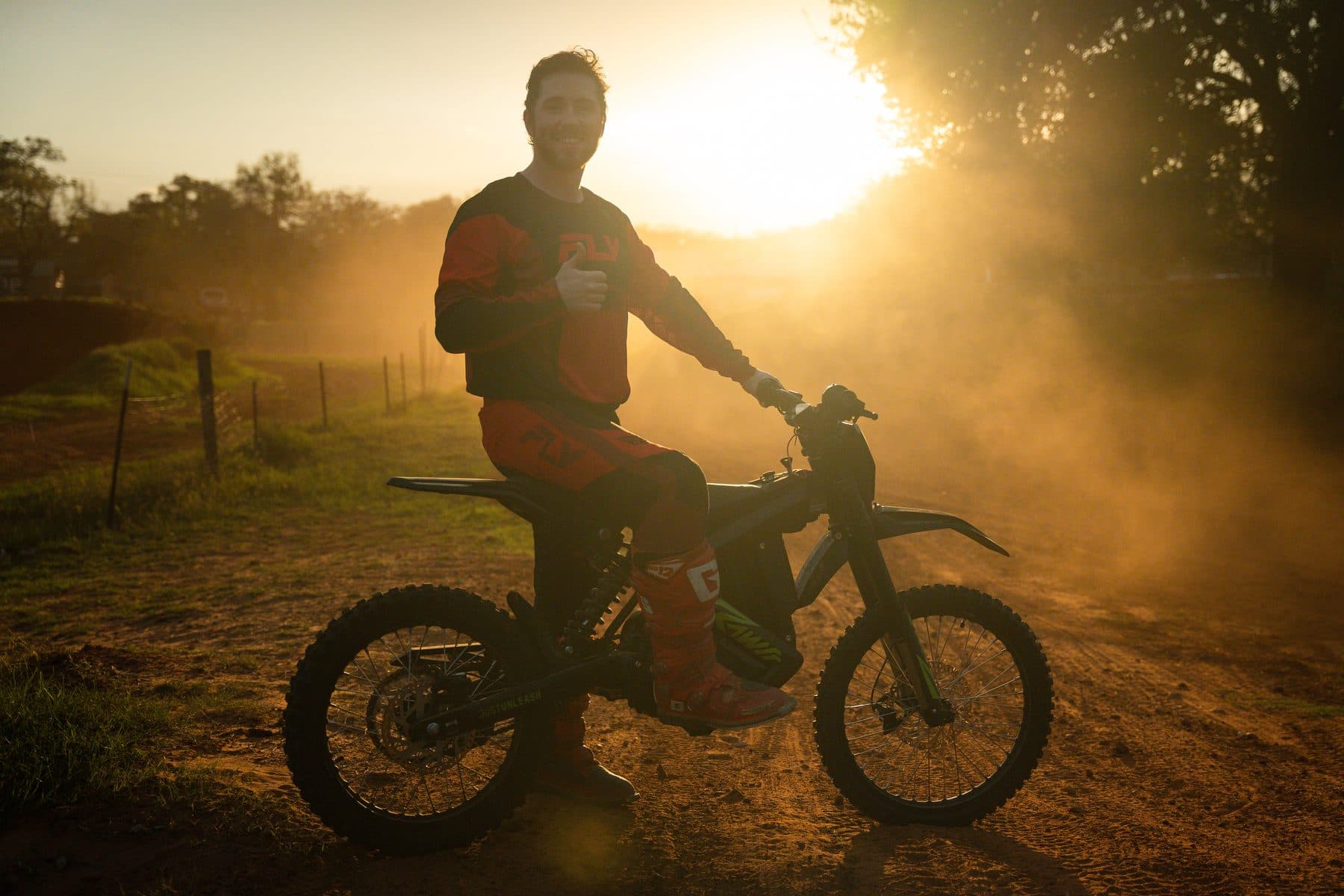 A smiling rider giving a thumbs-up on a dirt bike in golden-hour dust at Cycle Ranch