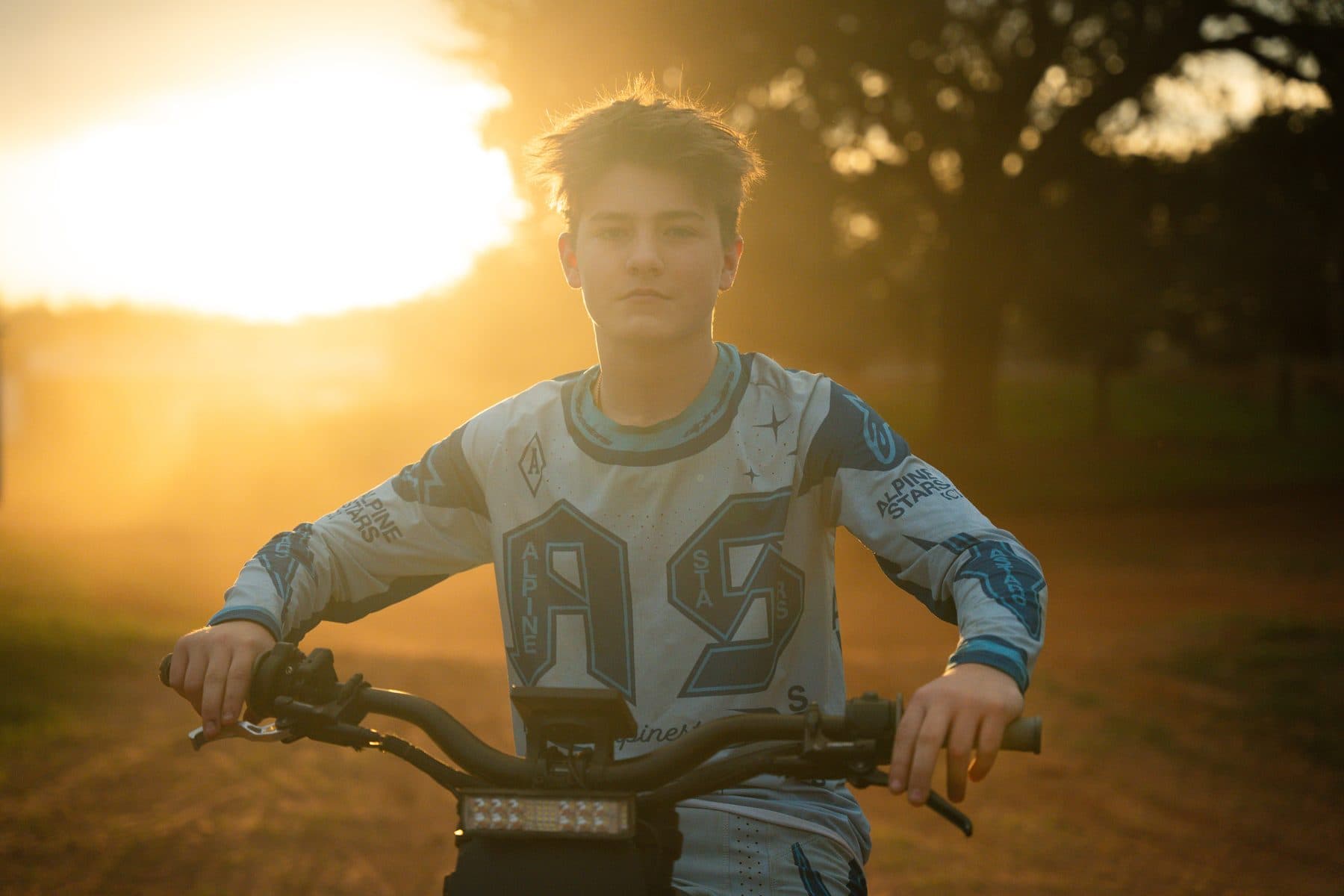 A young rider on a bike lit by warm golden-hour sun on a dirt path at Cycle Ranch