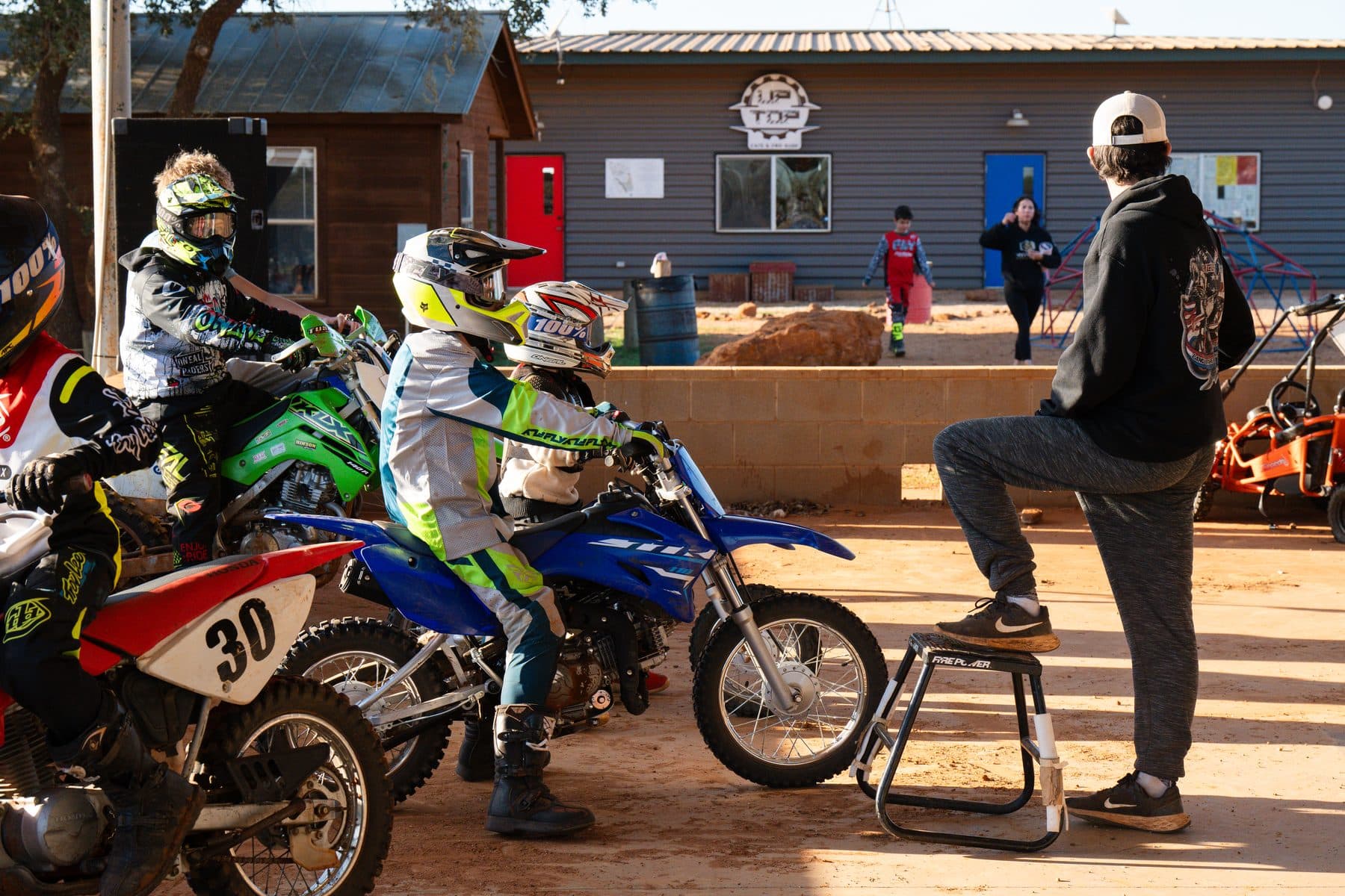 Young riders lined up on their bikes at the Cycle Ranch staging area while a coach looks on before heading out