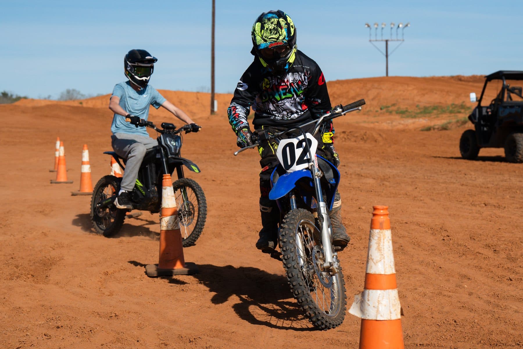 A first-time rider in a t-shirt learning to ride alongside a coached rider through cone drills on the Cycle Ranch track